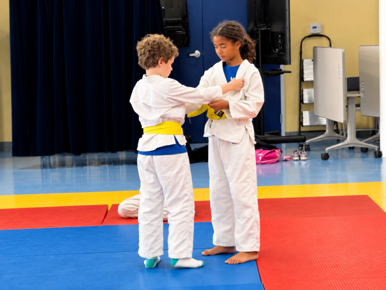 Dos alumnos con uniforme de judo atándose el cinturón